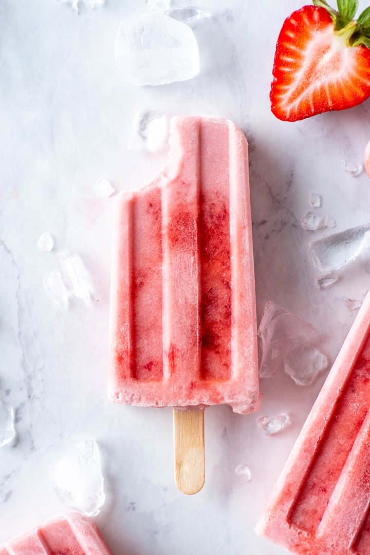 A single strawberry and coconut milk popsicle on a white background with a bite taken out of it