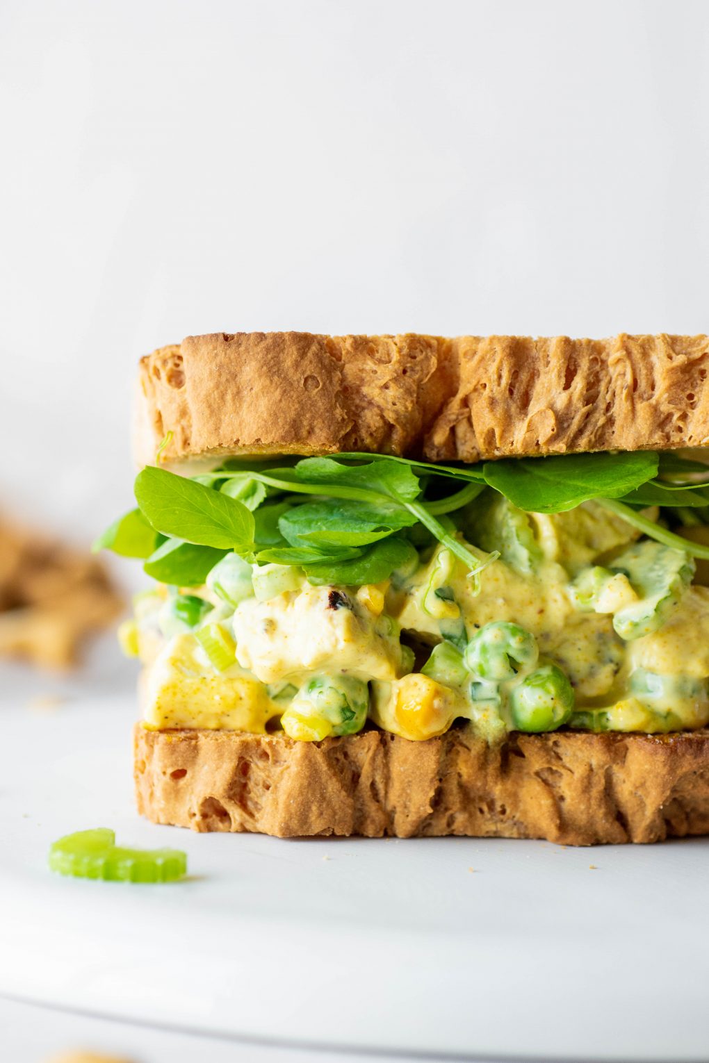 Close up side view of a chicken curry salad sandwich with bright greens on a white background.