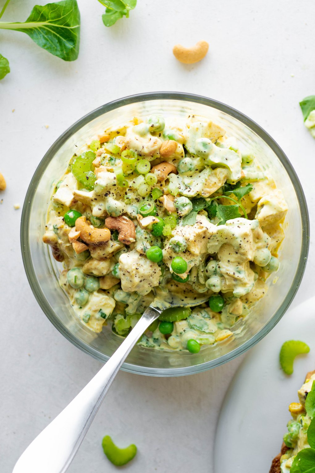 Overhead shot of a bowl of curried chicken salad with a spoon on a white background