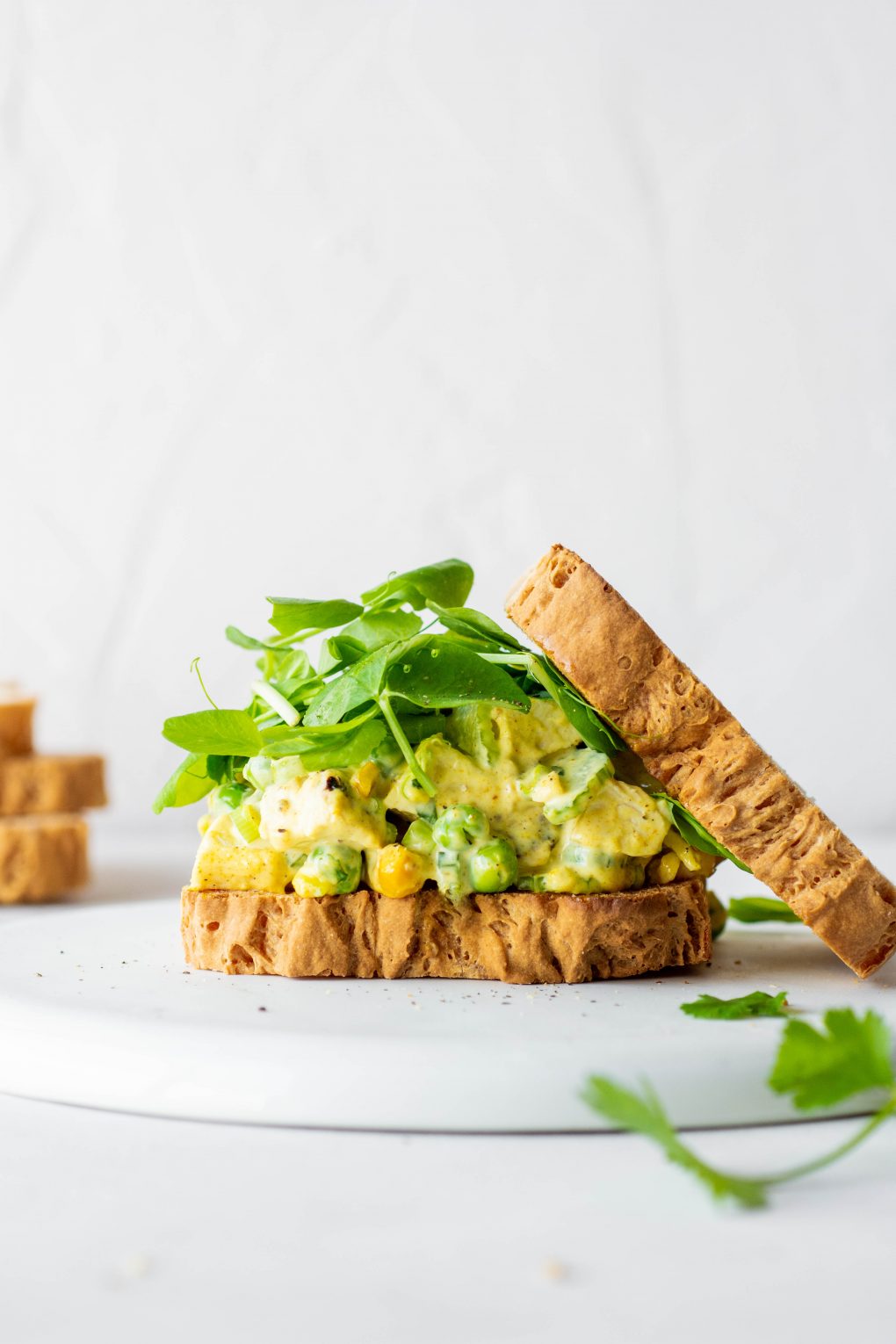 Side view of a curried chicken salad sandwich with some fresh greens and the top piece of bread angled off to the side. On a white background.
