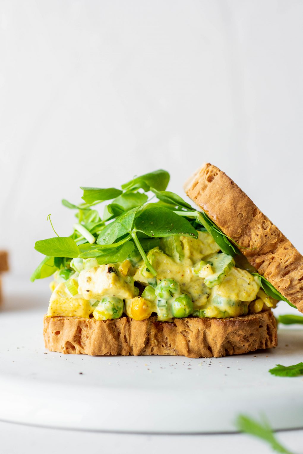 Side view of a curried chicken salad sandwich with some fresh greens and the top piece of bread angled off to the side. On a white background.