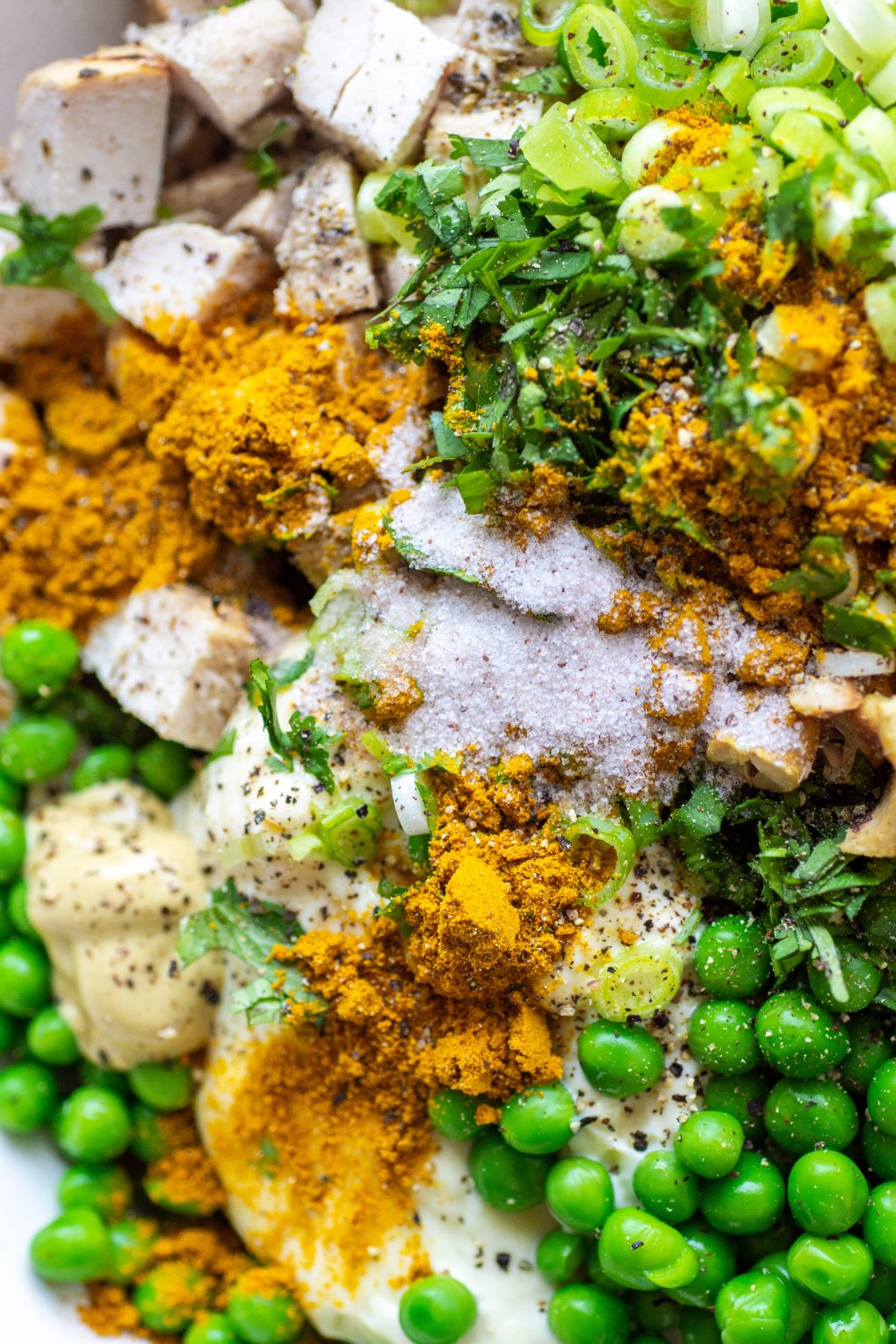 Overhead super close up view of curried chicken salad ingredients - chopped chicken, green peas, celery, green onions, cashews, mayo, and spices.