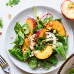 Close up view of a small plate of a green salad with peaches, chopped almonds, sliced onion, and crumbled feta cheese with mustard dressing