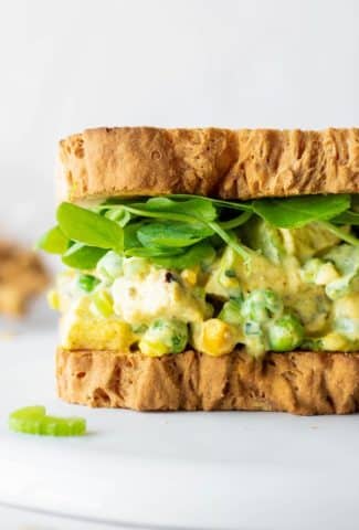 Close up side view of a chicken curry salad sandwich with bright greens on a white background.