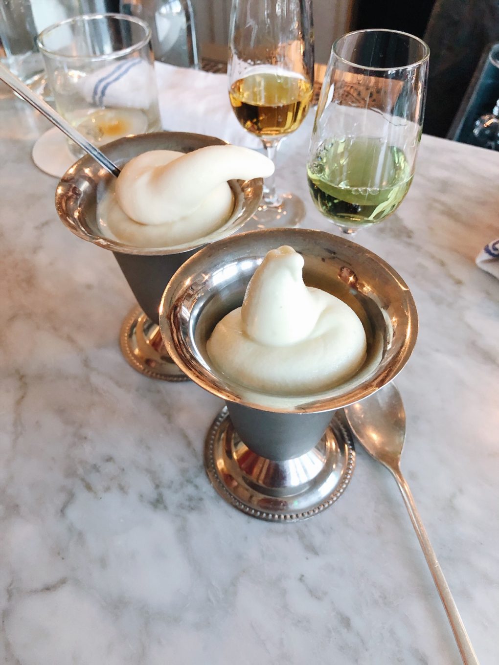 Two metal dishes of soft serve on a bar top next to two glasses of digestifs
