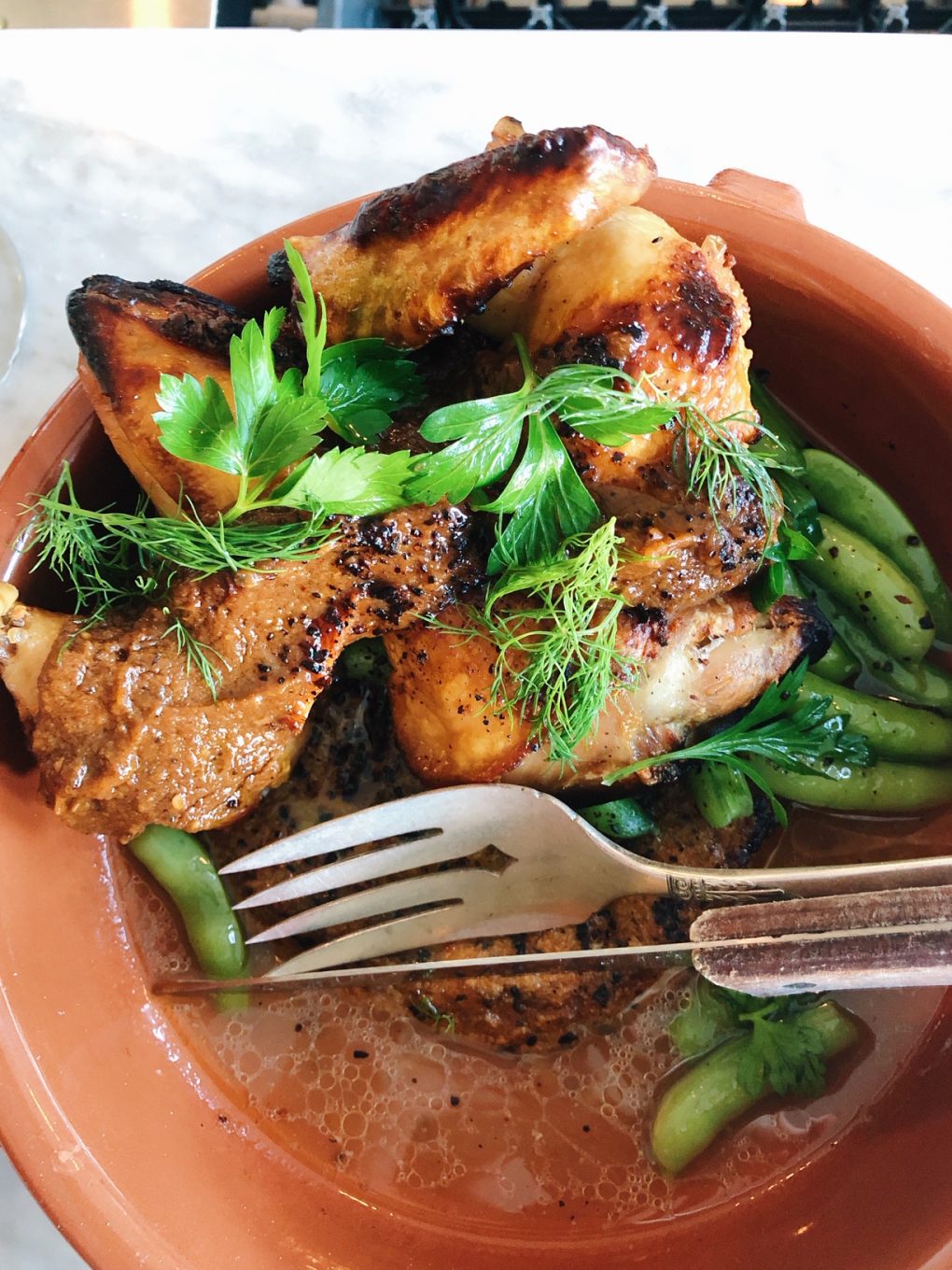 Roasted Chicken in a large bowl over a rice cake with fresh herbs on a white marble counter