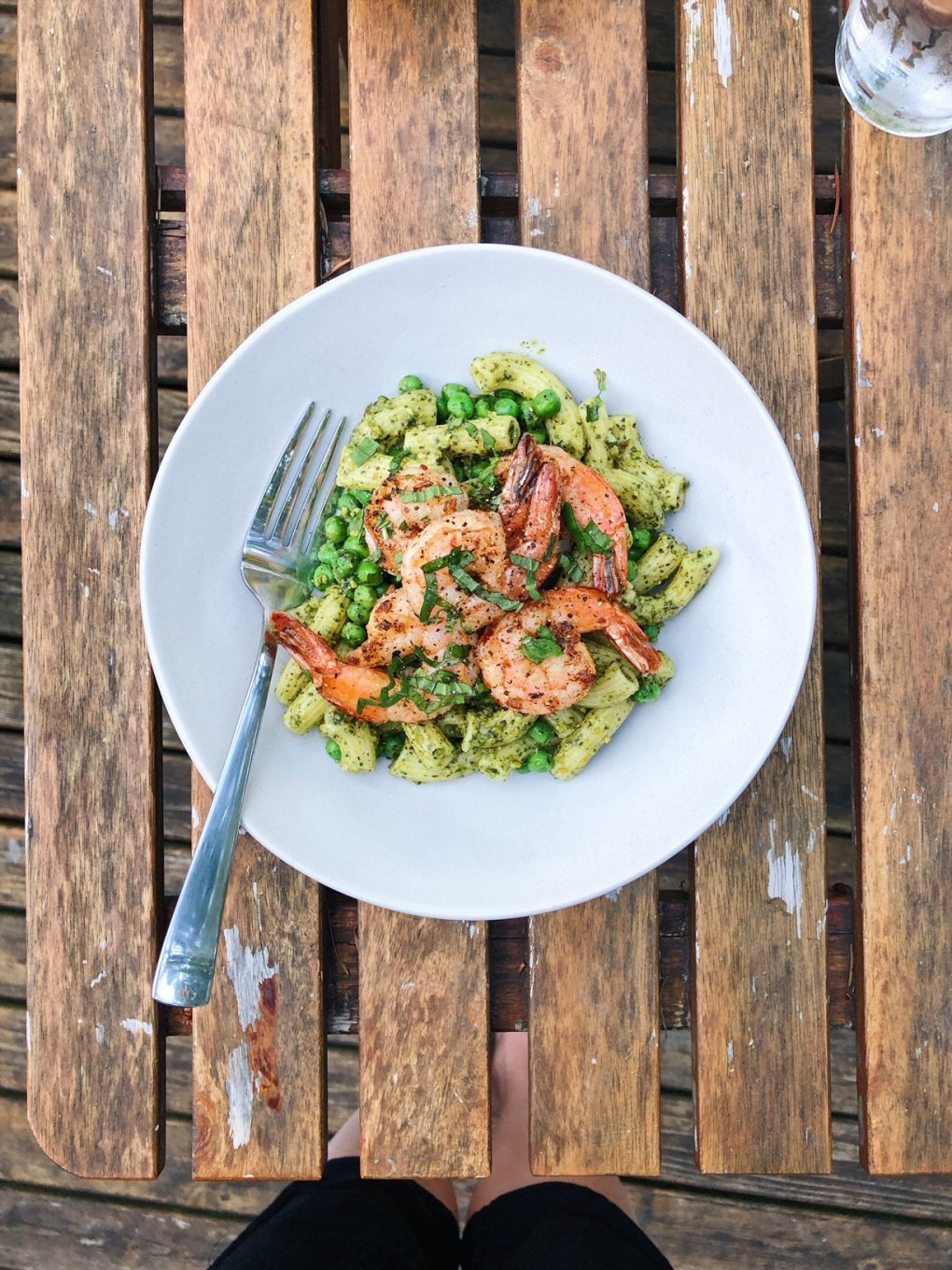 A white bowl filled with gluten free pesto pasta topped with seasoned shrimp on an outdoor table