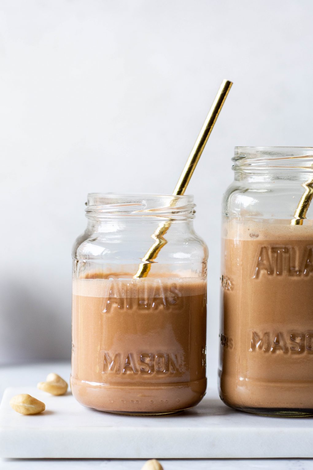 Close up side angle shot of two mason jars of chocolate cashew milk with gold straws on a white background