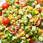 Colorful vegan chickpea salad on a large white speckled plate. Topped with fresh herbs and lemon wedges.