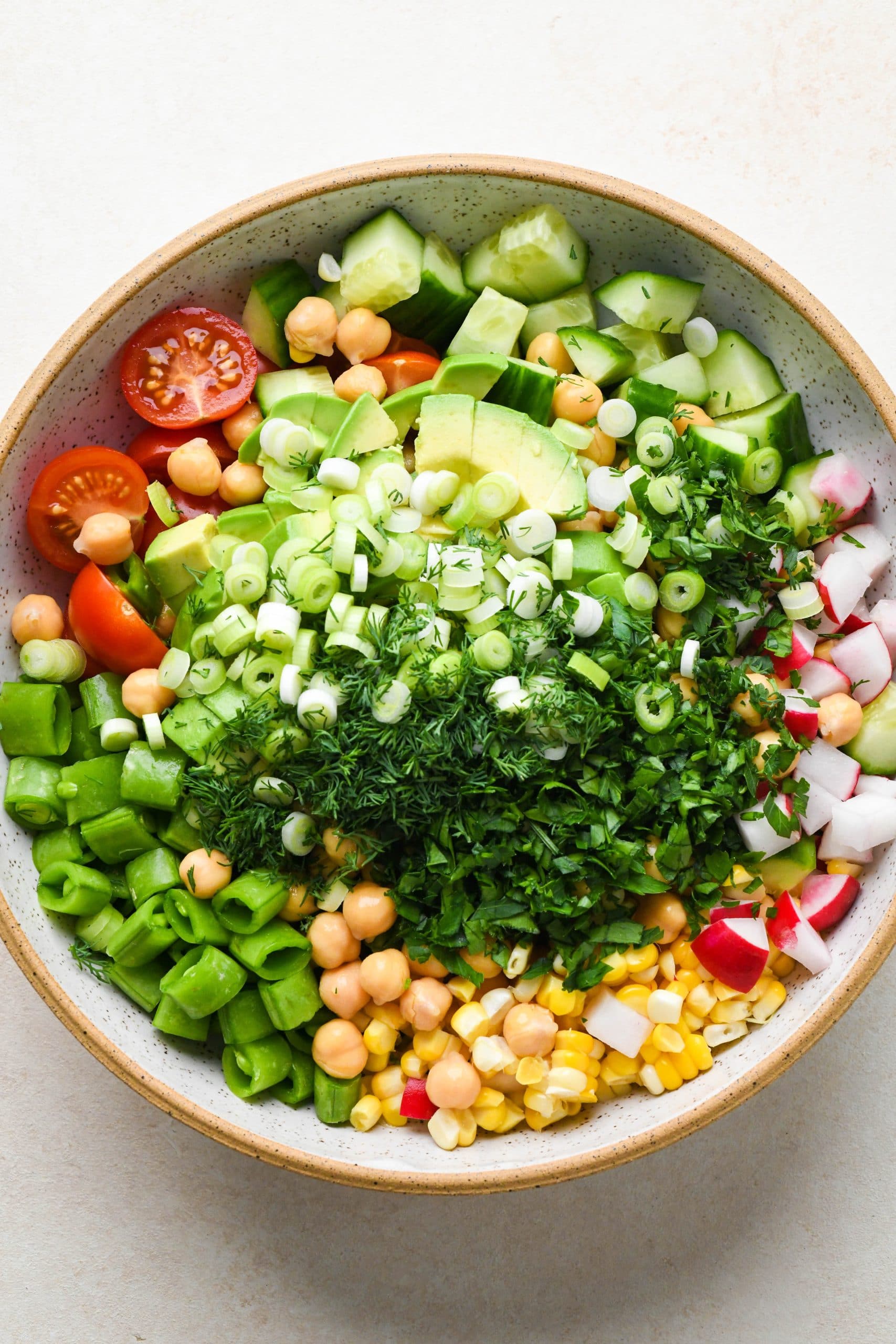 How to make vegan chickpea salad: Salad ingredients in a large bowl topped with fresh herbs and lemony dressing.