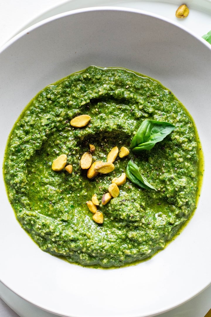 Close up of a white bowl of pistachio basil pesto topped with fresh basil and pistachios