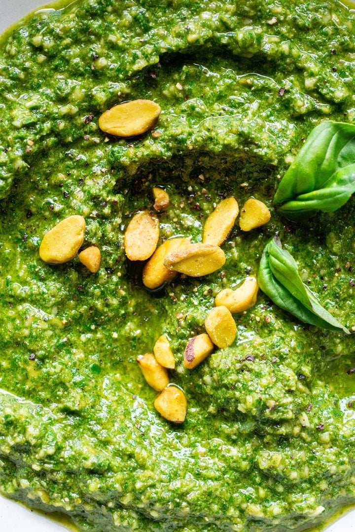 Super close up of a white bowl of pistachio basil pesto topped with fresh basil and pistachios