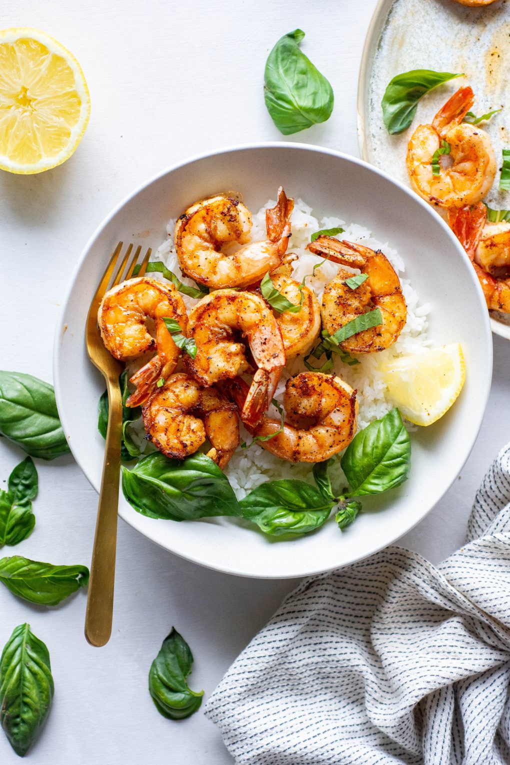 Large white bowl with white rice topped with seared shrimp with fresh basil and lemon wedges on a light background