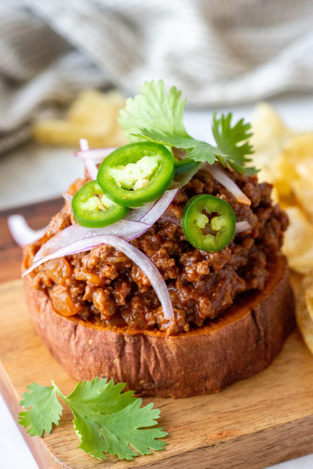 Close up 45 degree angle shot of an open faced sweet potato sloppy joe sandwich topped with jalapeno, cilantro, and red onion on a wooden board and white background