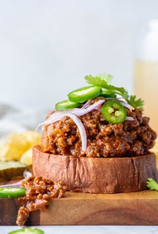 Close up side angle shot of a open faced sweet potato sloppy joe sandwich topped with cilantro, red onion, and jalapeno against a white background