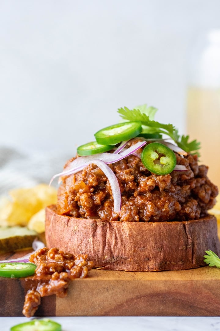 Close up side angle shot of a open faced sweet potato sloppy joe sandwich topped with cilantro, red onion, and jalapeno against a white background