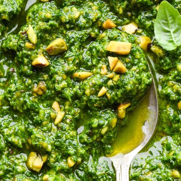 Close up image of a spoon dipping into bright green pistachio pesto to show the texture and bright green color.
