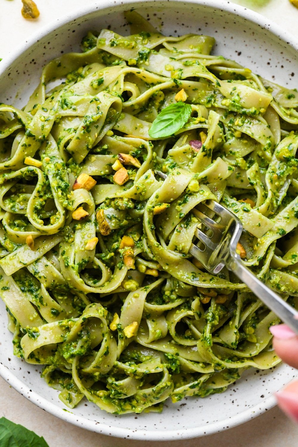 Pistachio pesto tossed with pasta in a shallow ceramic pasta bowl, topped with chopped pistachios and fresh basil leaves.