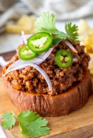 Close up 45 degree angle shot of an open faced sweet potato sloppy joe sandwich topped with jalapeno, cilantro, and red onion on a wooden board and white background