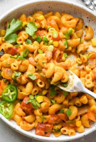 A shallow speckled bowl filled with vegan Mexican taco pasta topped with fresh herbs and jalapeño, with a fork scooping some out for a bite.