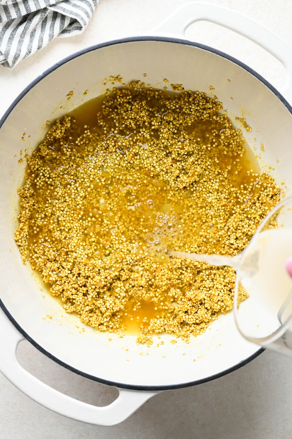 How to make curried quinoa pilaf: Pouring broth into the pot with quinoa and spices.