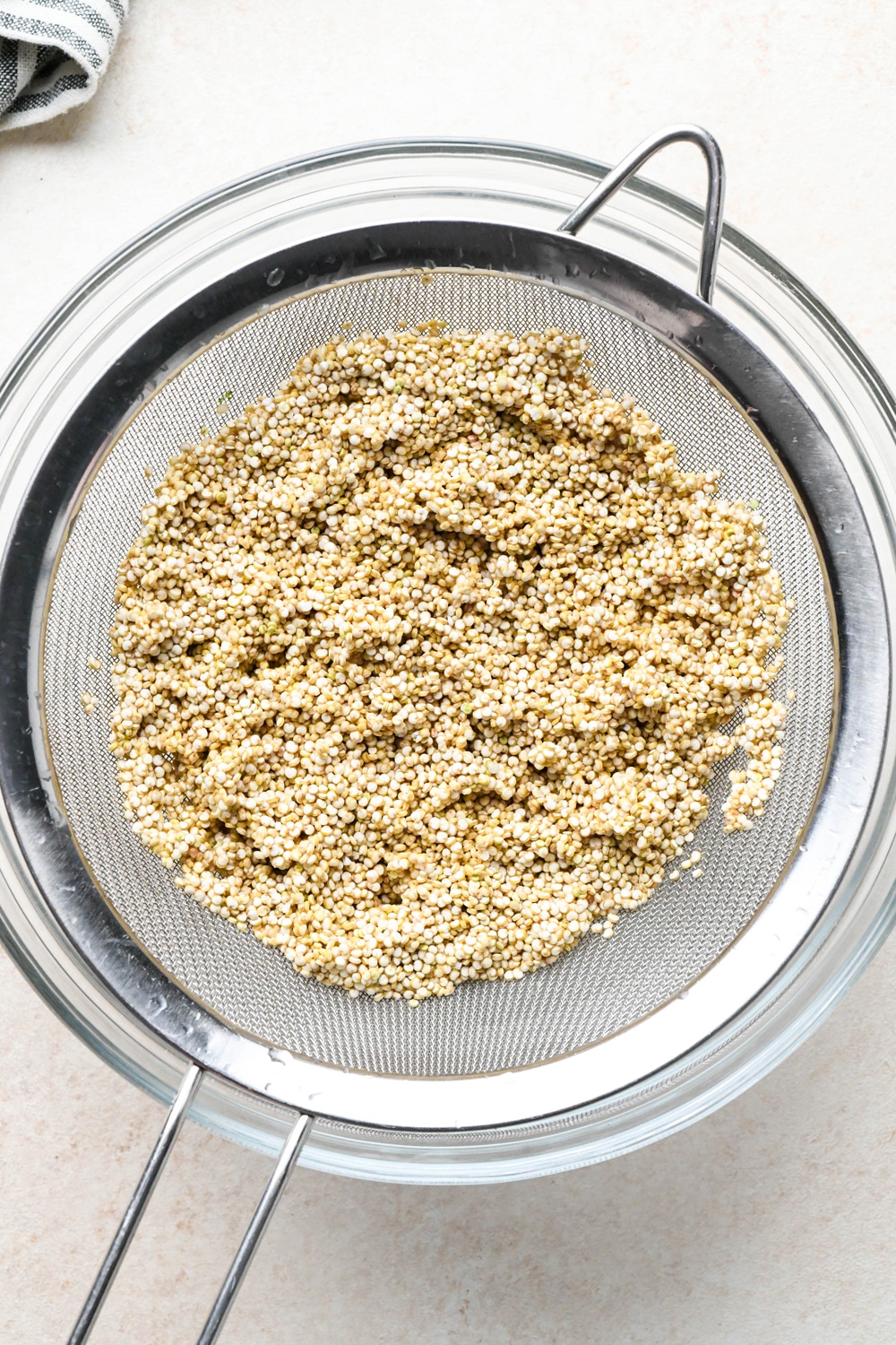 How to make curried quinoa pilaf: Quinoa rinsed and draining in a mesh strainer over a glass bowl.