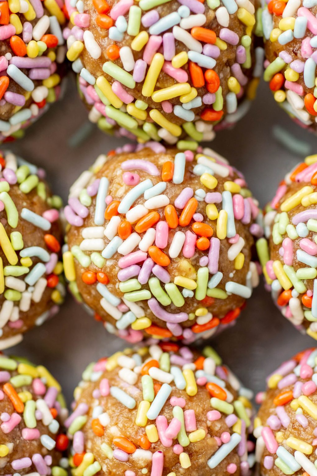 Super close up shot of rainbow sprinkle coated energy bites lined up next to each other.