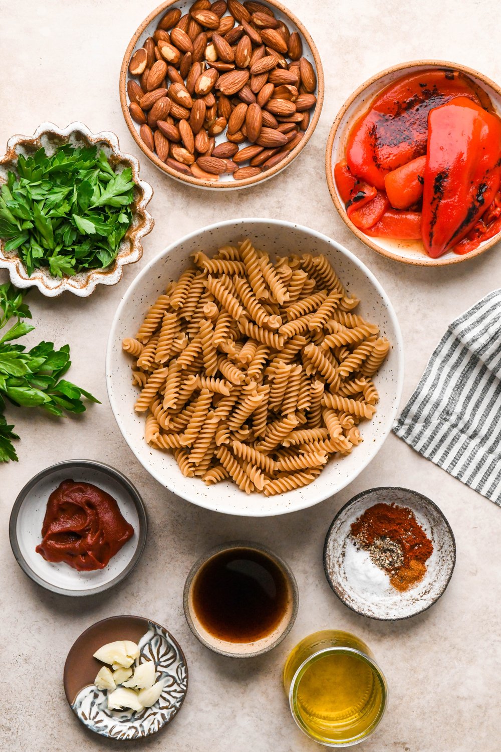 Ingredients for Quick Pasta with Homemade Romesco Sauce in various ceramics on a creamy light brown background. 