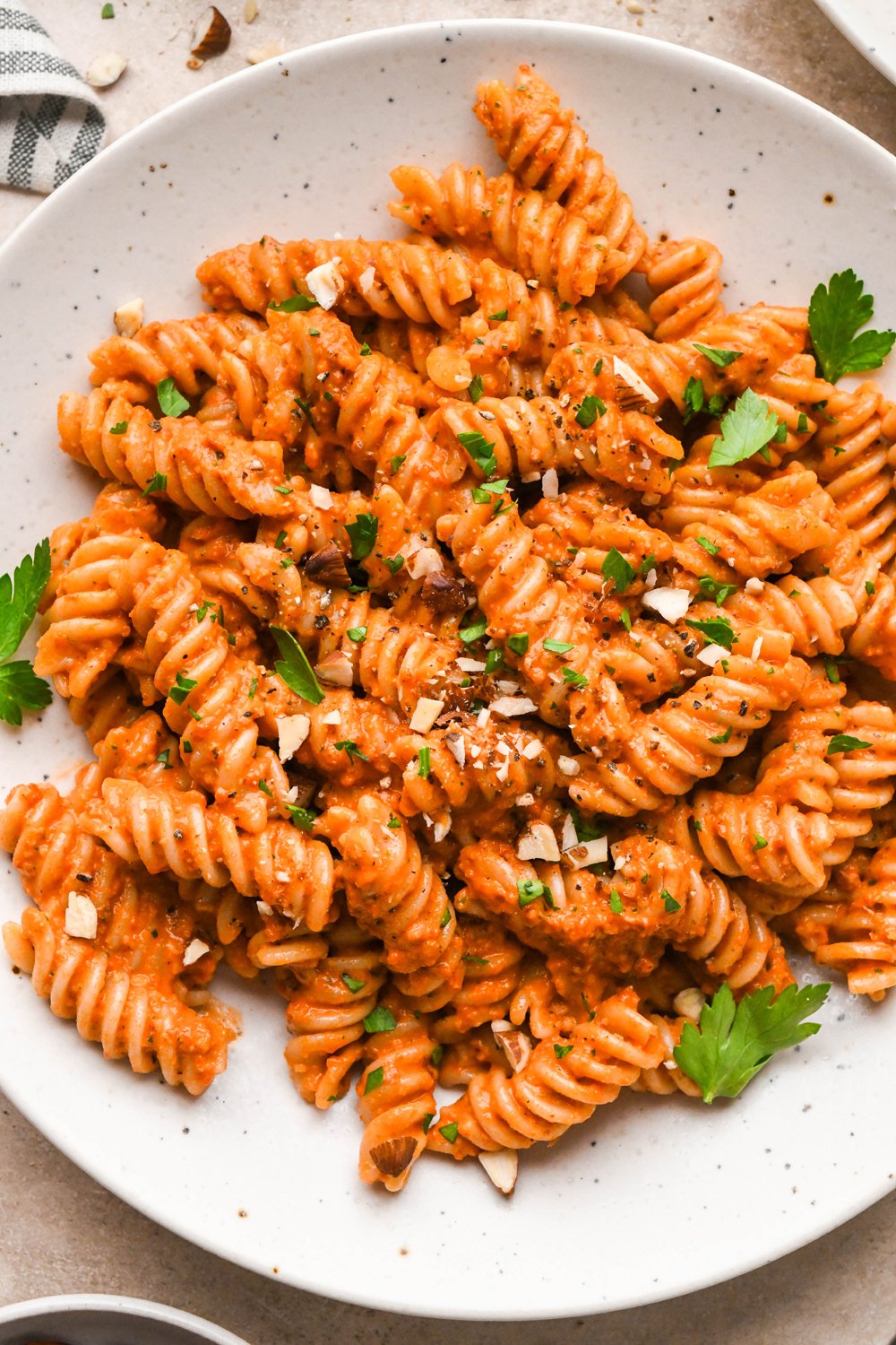 Romesco sauce tossed fusili pasta in a shallow speckled bowl, garnished with chopped roasted almonds and fresh parsley.