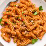 Romesco sauce tossed fusili pasta in a shallow speckled bowl, garnished with chopped roasted almonds and fresh parsley.