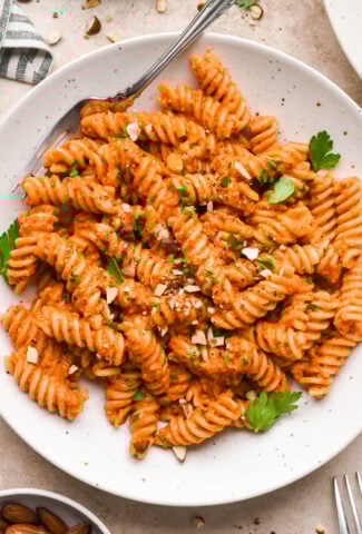 Romesco sauce tossed fusili pasta in a shallow speckled bowl, garnished with chopped roasted almonds and fresh parsley.