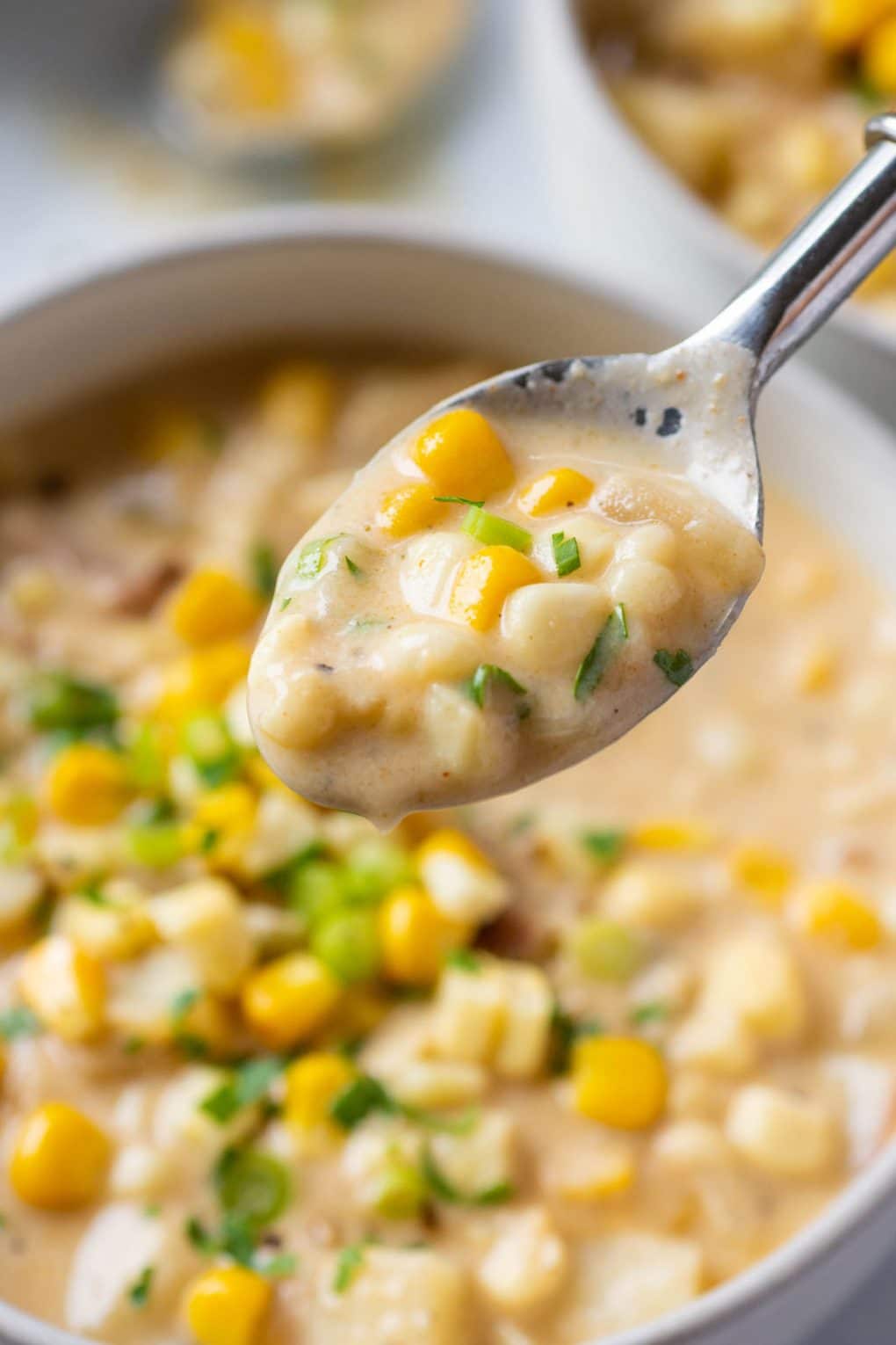 Close up shot of a spoon lifted out of a bowl of super creamy vegan corn chowder. On a light background. 