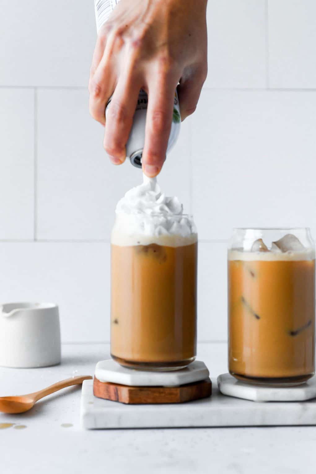 Straight on shot of latte being topped off with whipped cream from a canister. On a light colored background. 