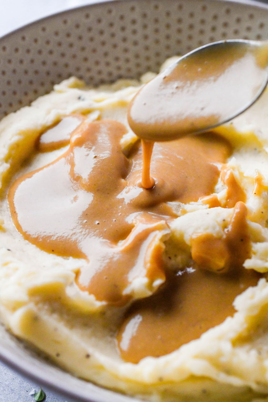 A close up shot of a spoon drizzling luscious gluten free gravy over mashed potatoes. 