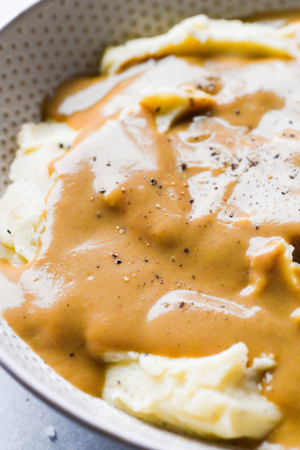 Close up shot of super easy gluten free gravy draped over mashed potatoes, and topped with some cracked black pepper. 