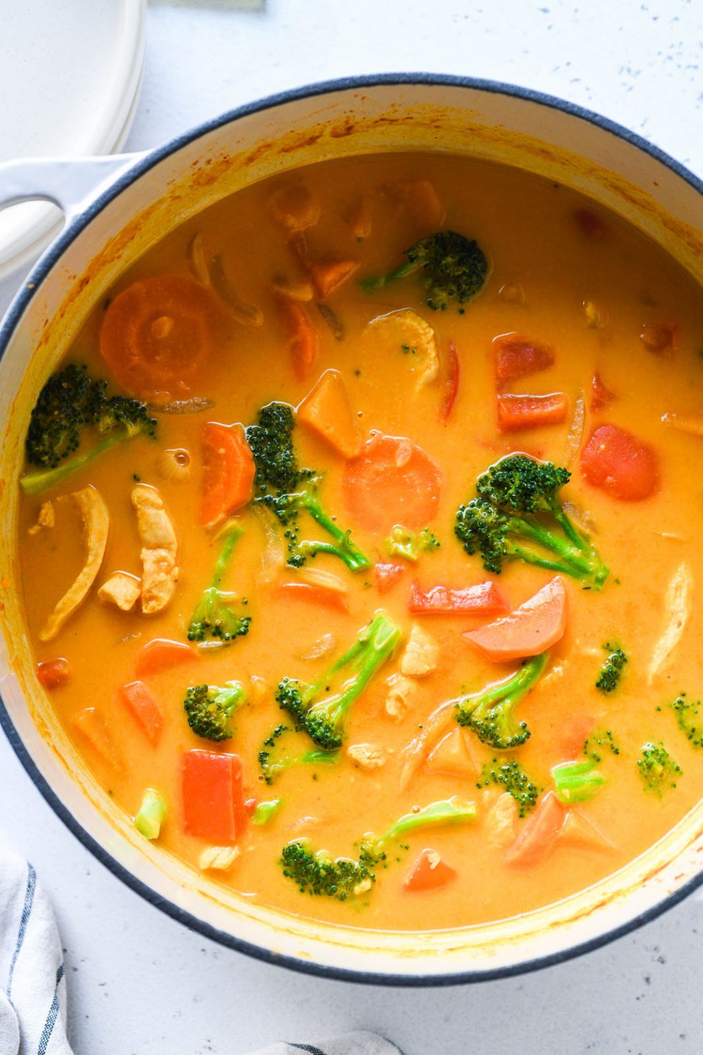 Overhead shot of a large pot full of brothy bright orange pumpkin curry. Curry has sliced carrots, pieces of red pepper, broccoli, and chicken in it.