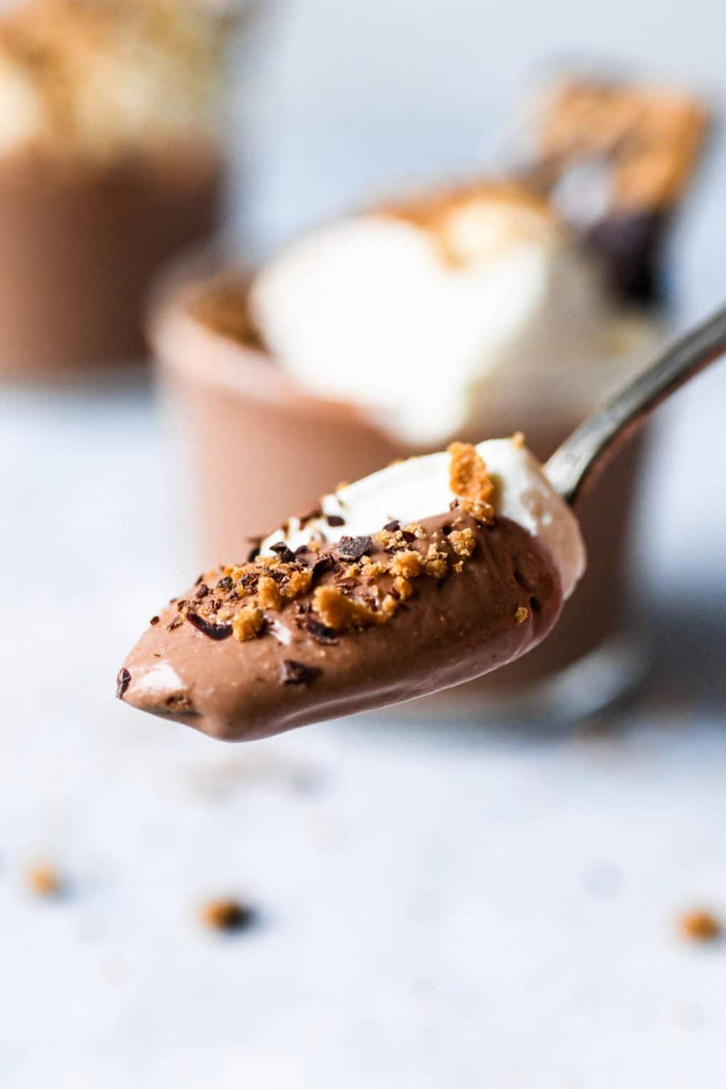 Close up shot of a spoon filled with dairy free chocolate mousse, whipped cream, and graham cracker crumbs.