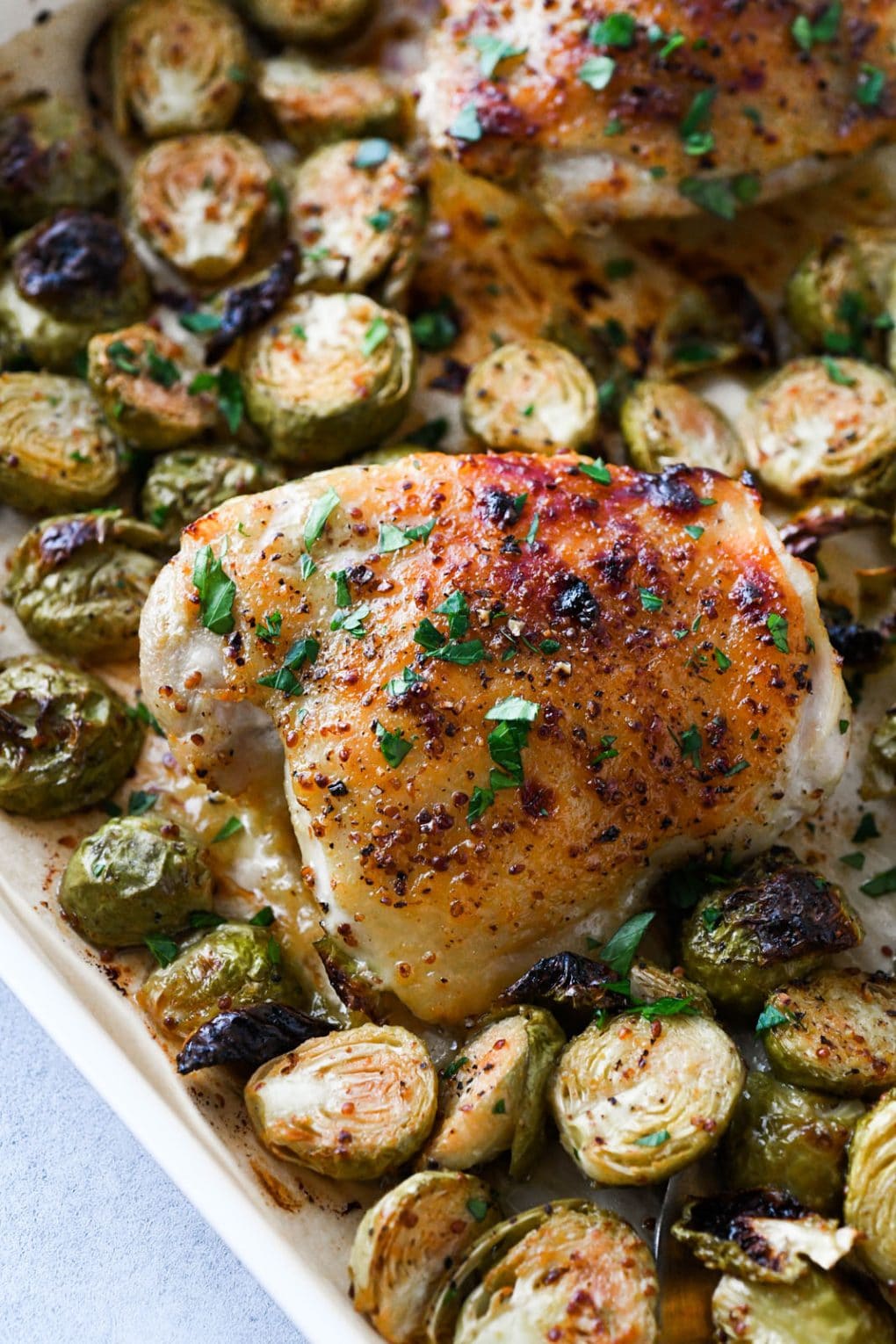 Close up shot of a honey mustard glazed chicken breast. On a sheet pan nestled amongst crispy roasted brussels sprouts