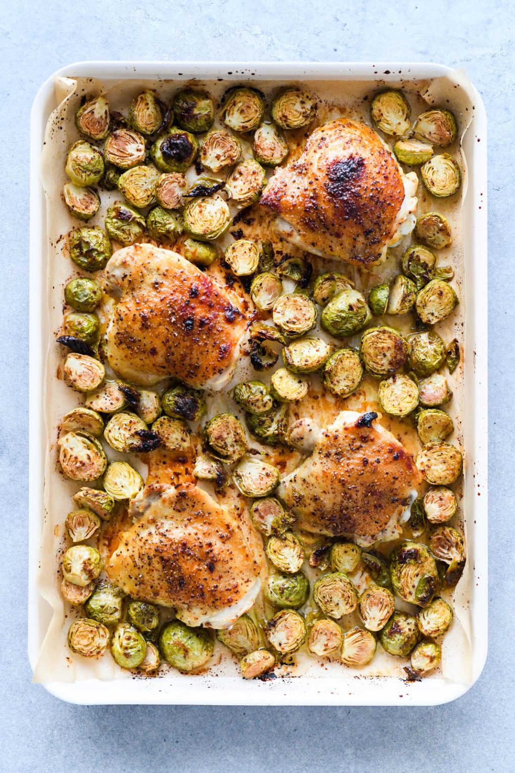 Overhead view of a sheet pan with four golden brown honey mustard glazed chicken thighs, surrounded by crispy roasted brussels sprouts