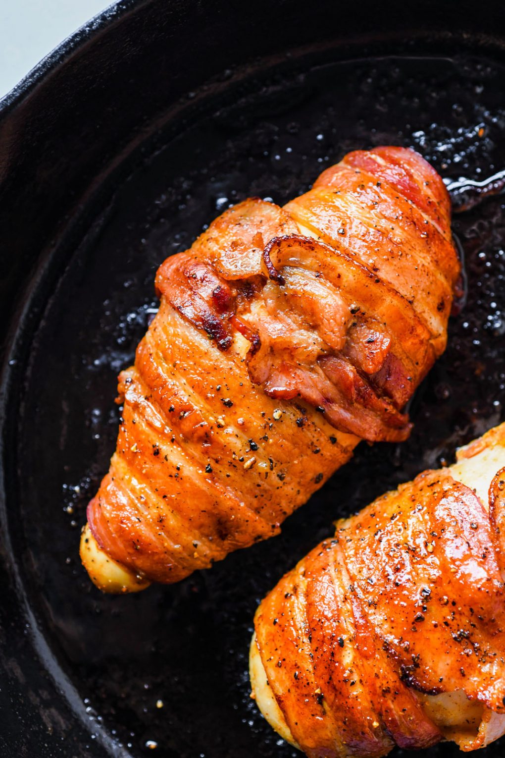 Close up shot of two baked golden brown bacon wrapped chicken breasts in a cast iron skillet. 