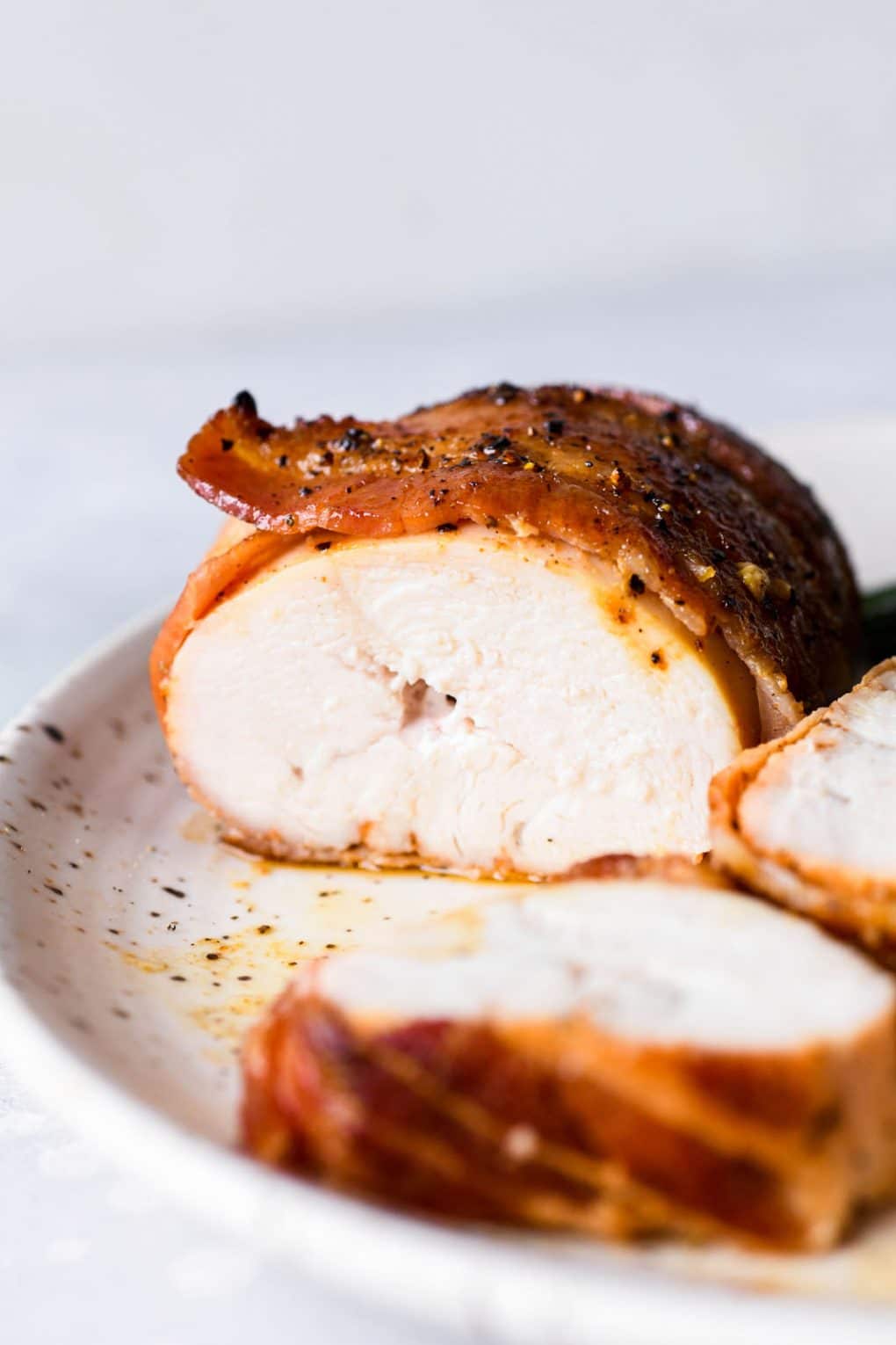 Close up shot of the interior of a bacon wrapped chicken breast on a light colored speckled plate, with a bright light colored background. 