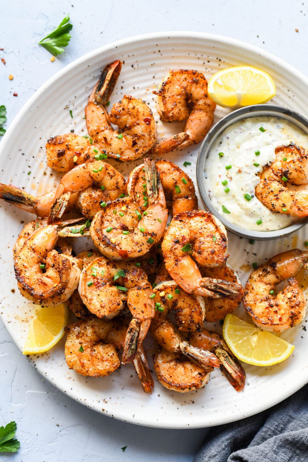 Light speckled plate of cajun spiced shrimp topped with snipped chives. Lemon wedges on the plate and a small bowl of aioli. 