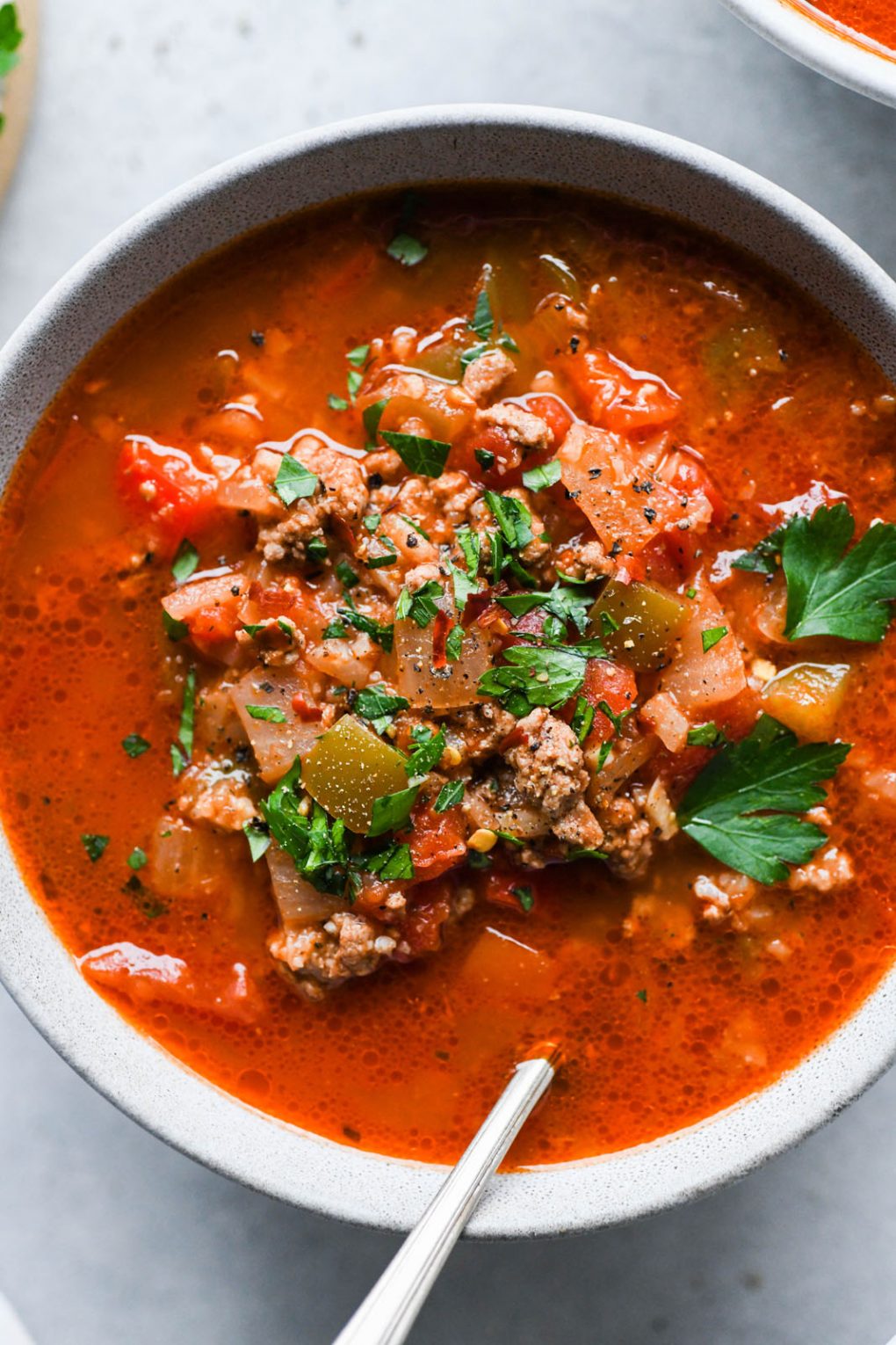 Close up overhead shot of a colorful bowl of stuffed pepper soup on a light background.