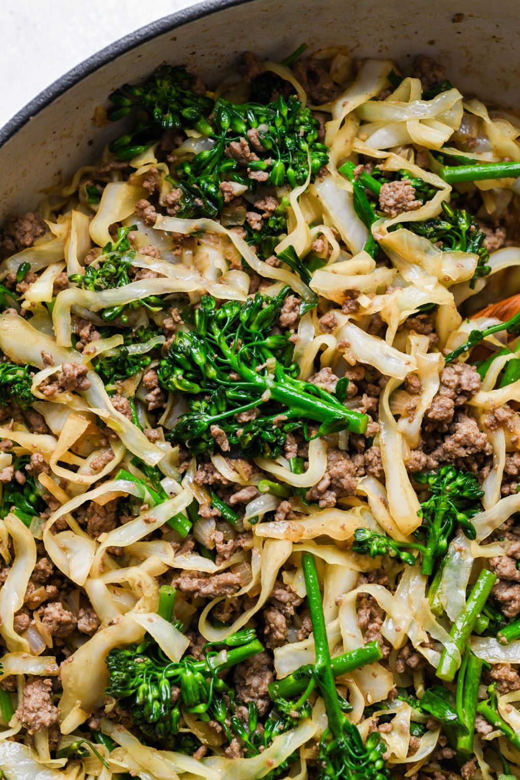 Close up shot of cooked Whole30 ground beef stir fry with cabbage - also contains bright green pieces of broccolini.