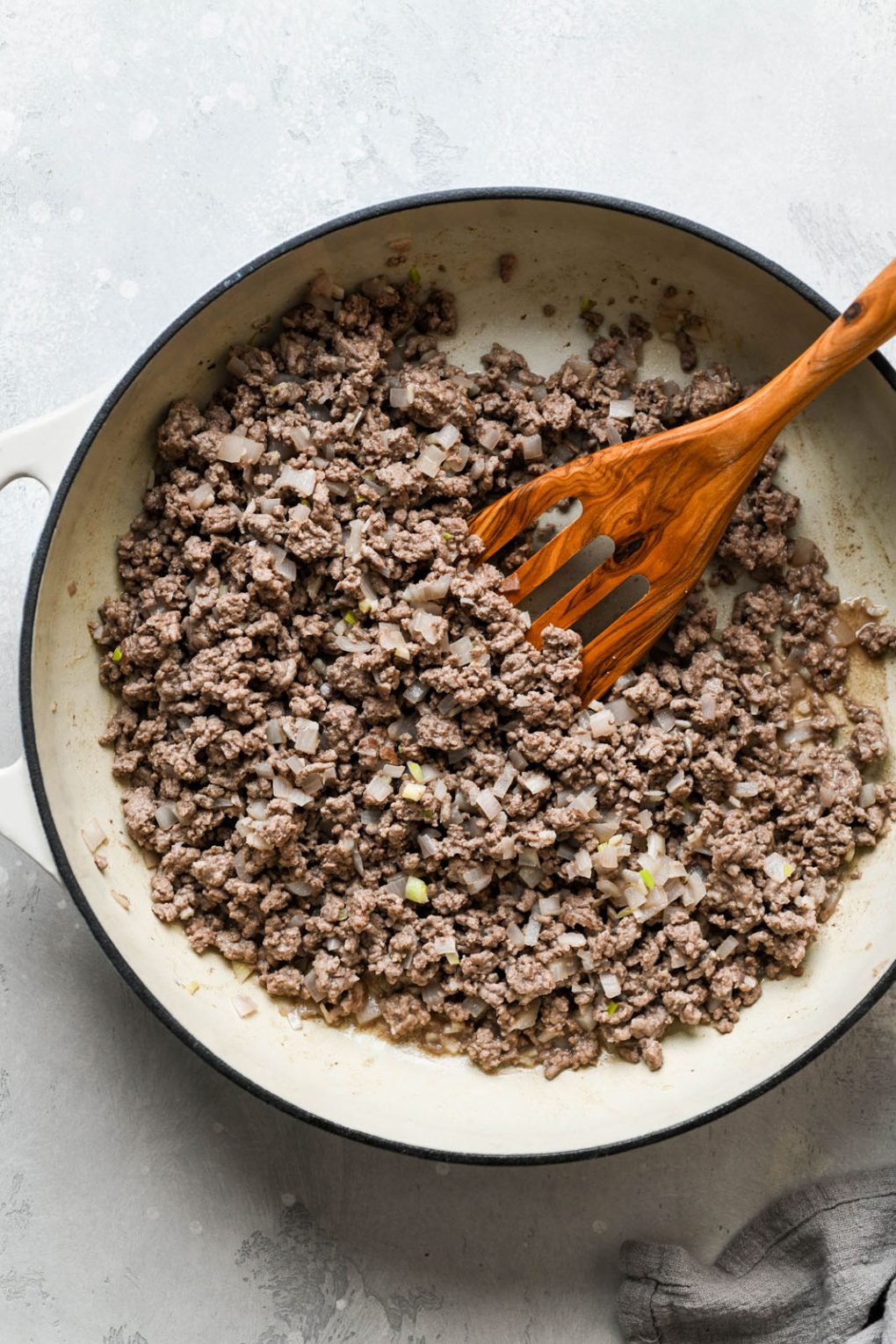 Overhead shot of a cream colored ceramic skillet filled with cooked ground beef, shallots, and garlic. 