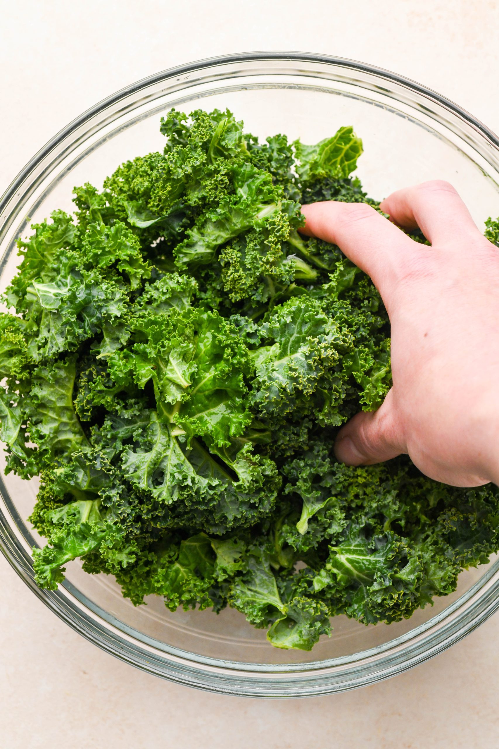 How to make Kale Chicken Caesar Salad: A large bowl of kale leaves, being massaged by a hand.