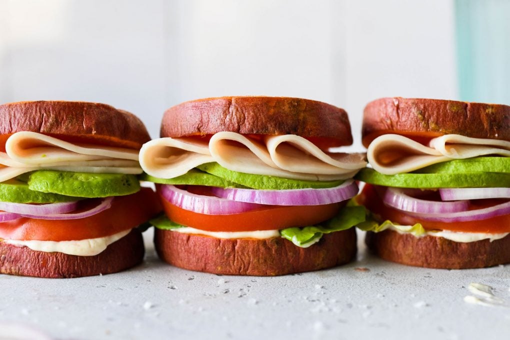 Straight on picture of three little deli style turkey sandwiches in a row made with roasted sweet potato rounds as buns. 