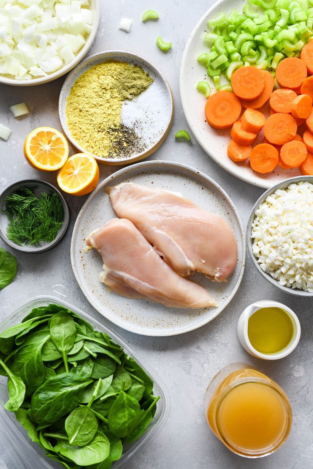 Overhead image of all the ingredients needed for nourishing chicken and cauliflower rice soup - raw chicken breasts, cauliflower rice, sliced carrots, celery, diced onion, and baby spinach. 