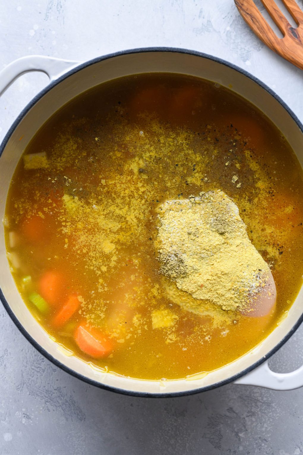 Overhead shot of a large white ceramic soup pot filled with broth, chicken breast, and spices.