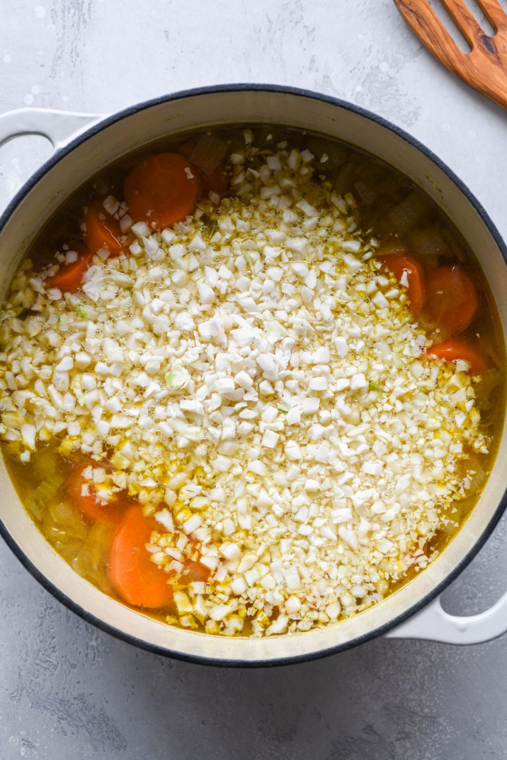 Overhead shot of a large white ceramic soup pot filled with broth, chicken breast, and spices - filled with cauliflower rice.